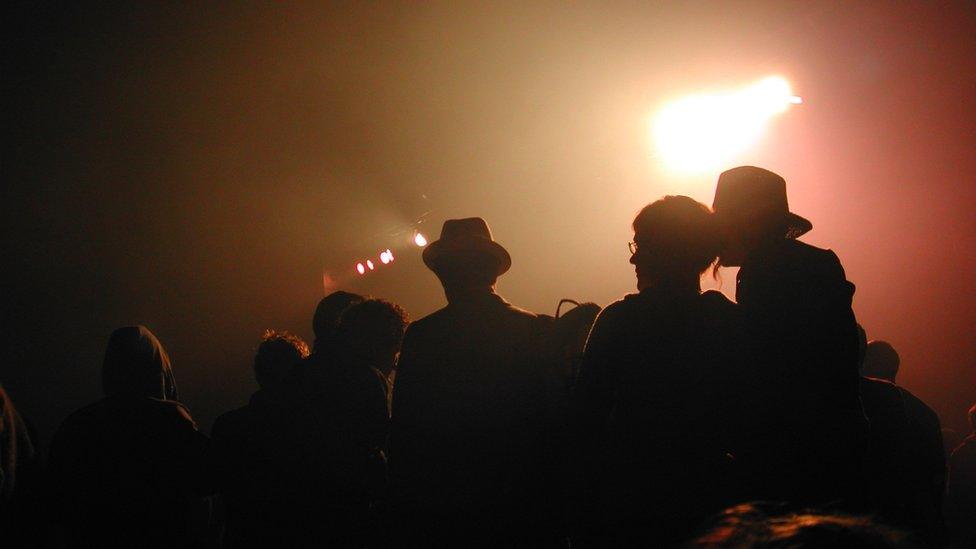 People are silhouetted against the light at the start of a gig