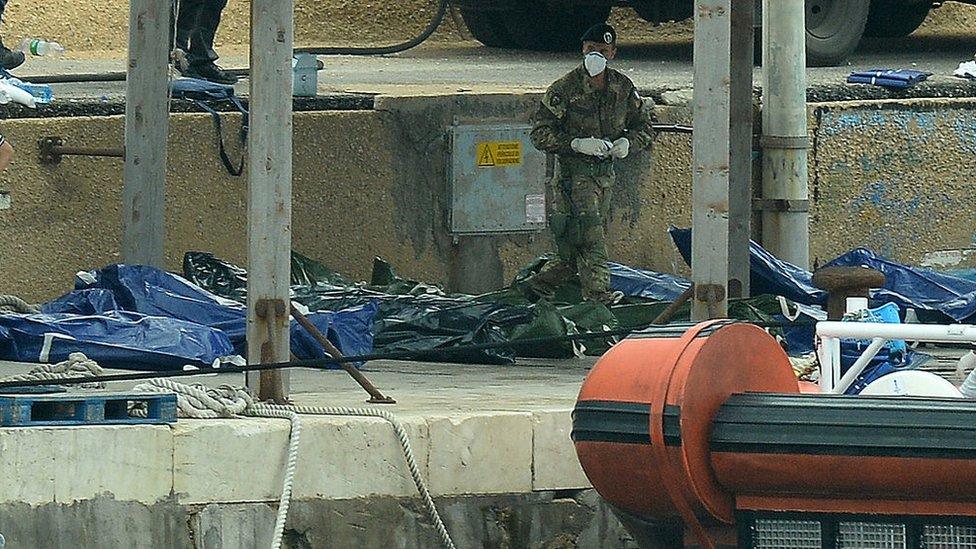 An officer stands over the bodies of some of the African migrants killed in a shipwreck off the Italian coast in the harbour of Lampedusa