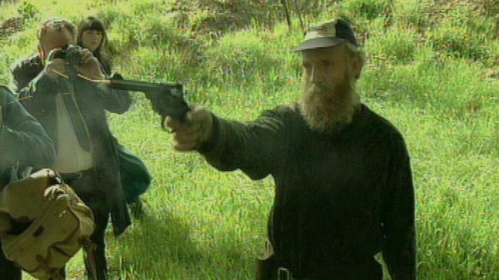 Albert Dryden holding his gun while journalists look on