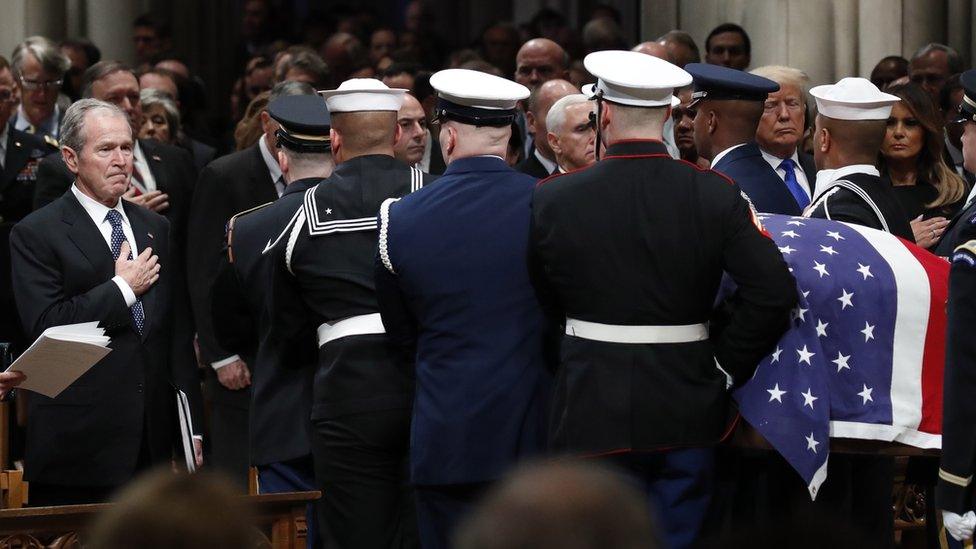 George W Bush places his hand on his chest as his father's casket is carried from the cathedral