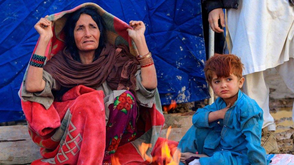 Afghans warm themselves at a fire outside their home destroyed