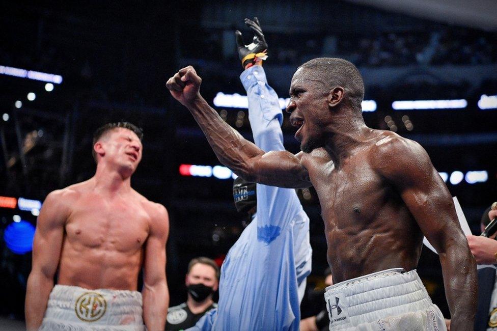 A boxer lifts his fist in jubilation as his opponent scrunches his face up in dismay.