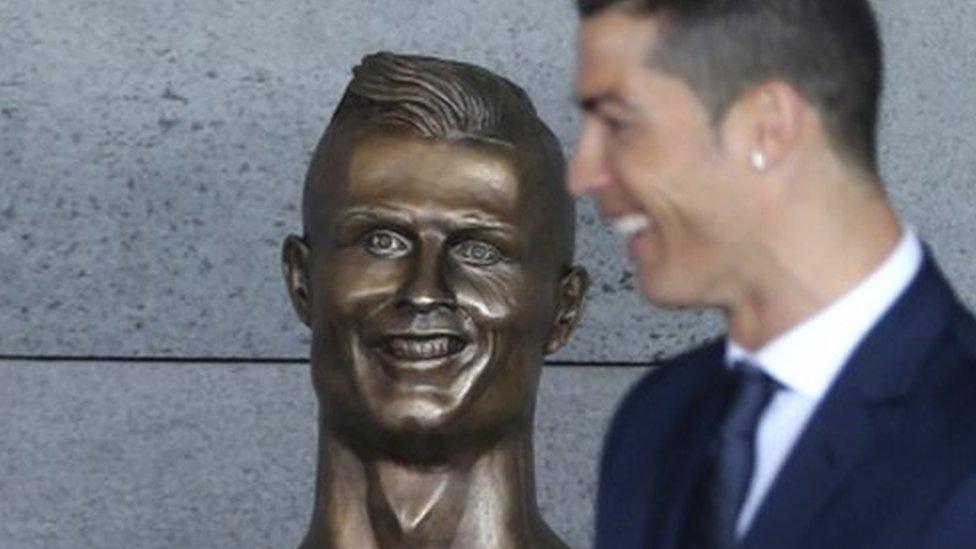 Ronaldo stands out of focus in front of his bust at the airport