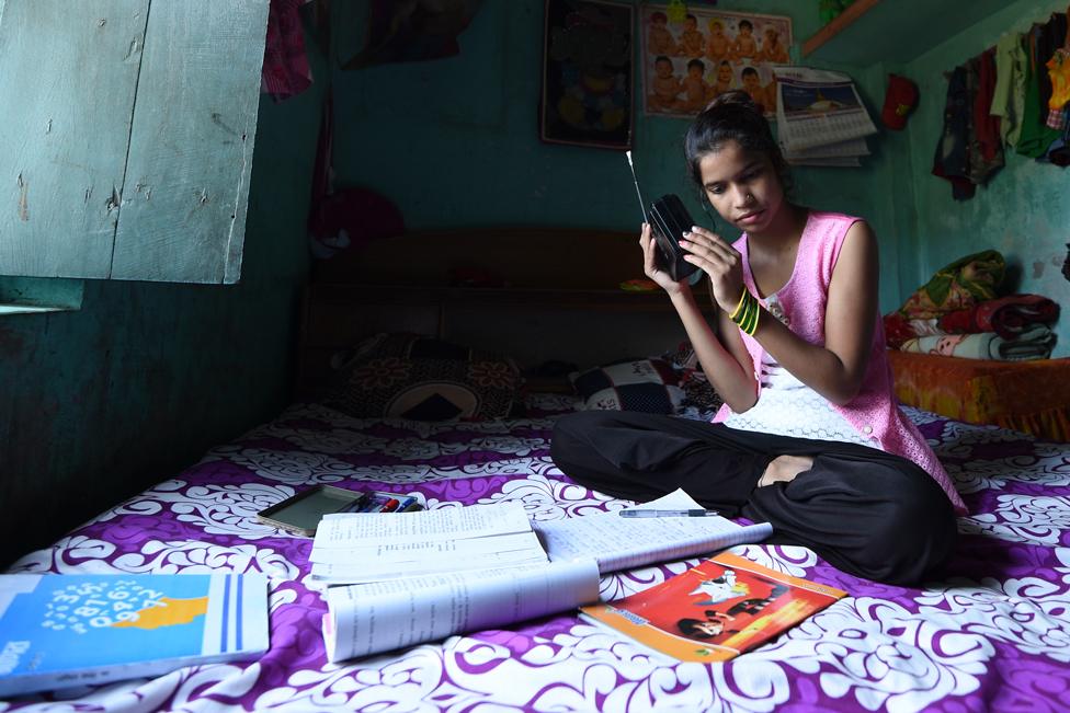 Anjali Patel holding a radio with sheets of paper surrounding her