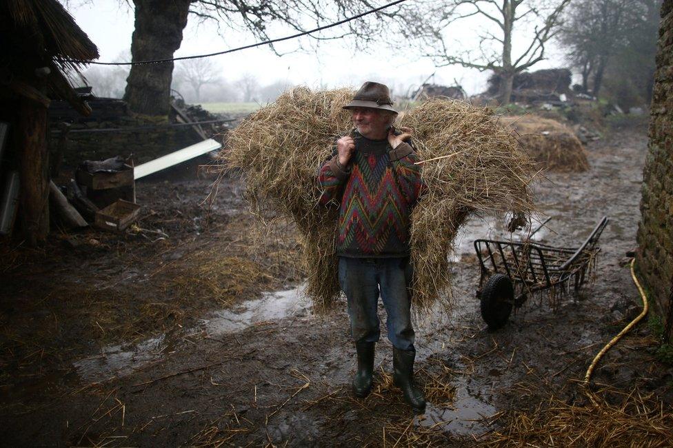 Farmer Jean-Bernard Huon stands on his farm with a bail of hay on his back.