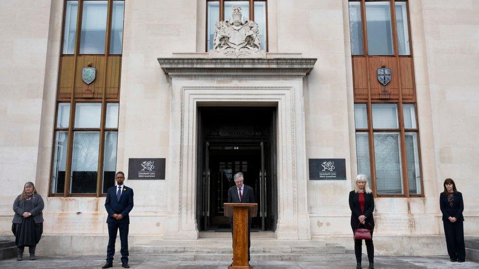 First Minister of Wales Mark Drakeford (centre) takes part in a minutes silence on the steps of the Welsh Government Building in Cathays Park with Julie James MS (far left), Vaughan Gething MS (2nd left) Dame Shan Morgan (fourth from left) and Lesley Griffiths MS (right) on March 23, 2021 in Cardiff, United Kingdom