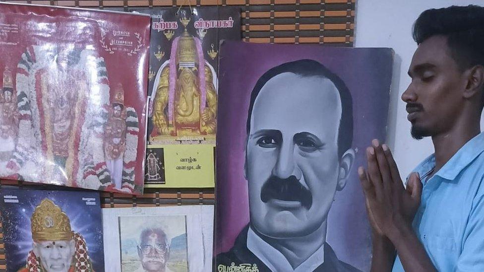 20-year-old student offering prayers in front of images of Hindu gods and the colonial engineer John Pennycuick