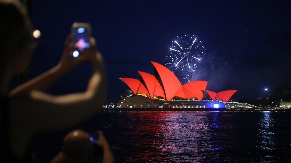 Spectators take photos of fireworks as they explode behind the Sydney Opera House as it glows red as part of celebrations for Chinese Lunar New Year of the pig, in Sydney