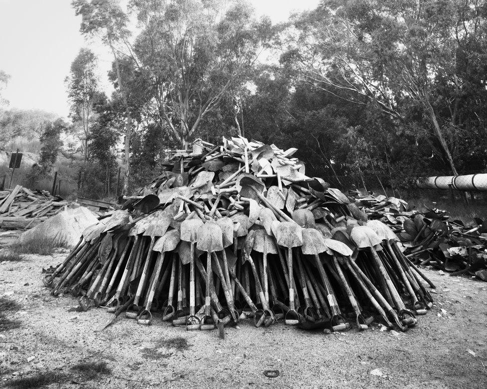 "Lashing" shovels retrieved from underground. Every grain of sand in the yellow tailings dumps that made the Witwatersrand landscape and every grain of gold that made its wealth, came from a rock off a black man's shovel underground. Central Salvage Yard, Randfontein Estates, Randfontein, 1966 .