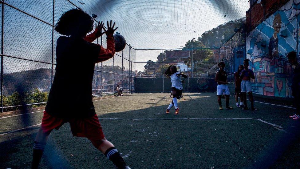 Seen from behind the goal, one of the girls takes a shot on target into the goalkeeper's waiting hands, as others watch nearby