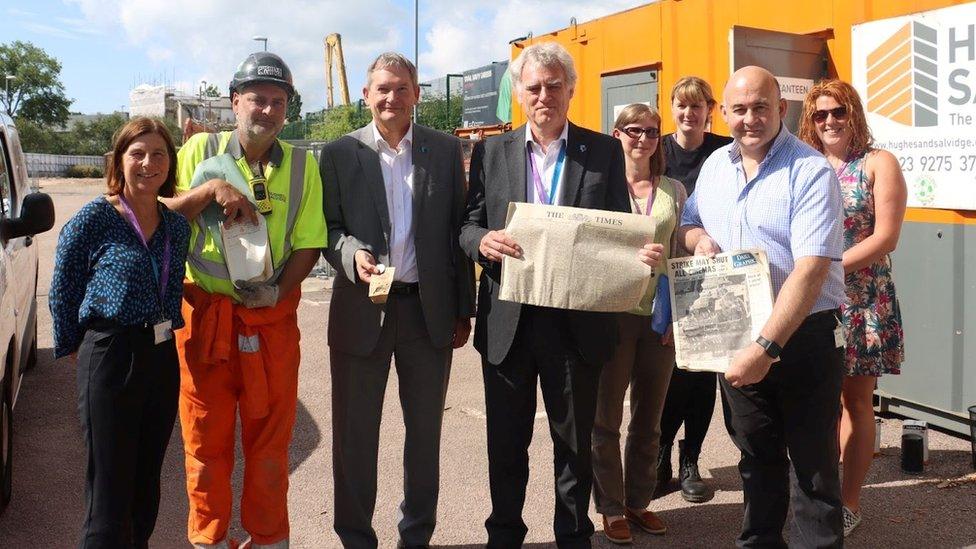 a group of eight people holding items like old newspapers