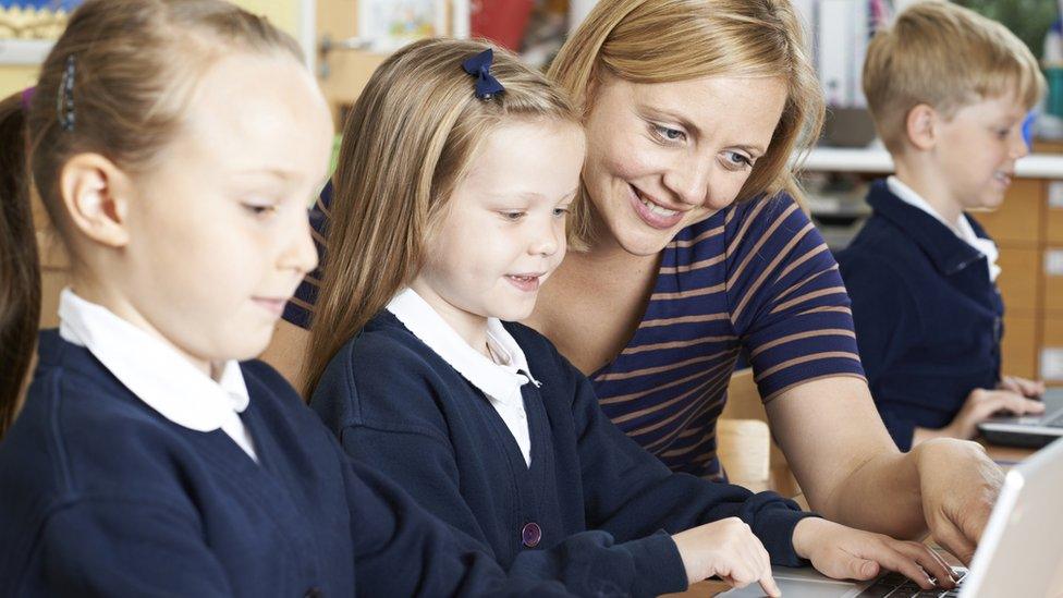 Women helps two young girls with a laptop computer in a classroom