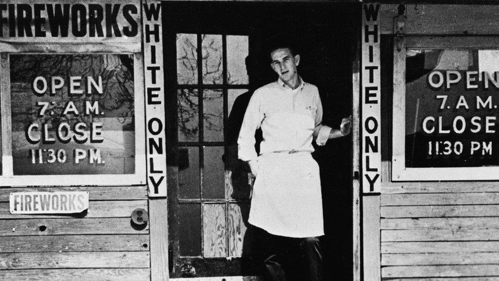 A man stands in the doorway of a store marked 'White Only' in the United States around 1950