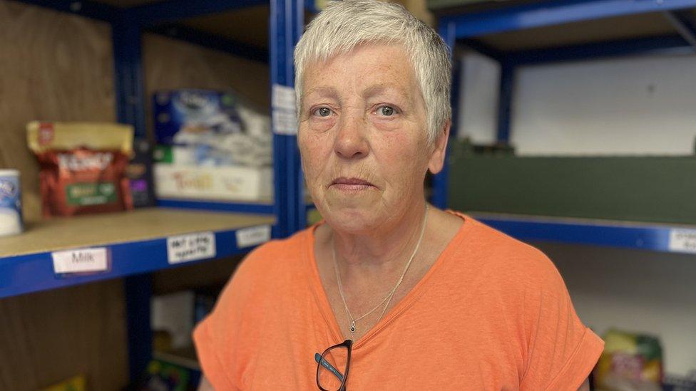 A woman in an orange top next to empty food shelves