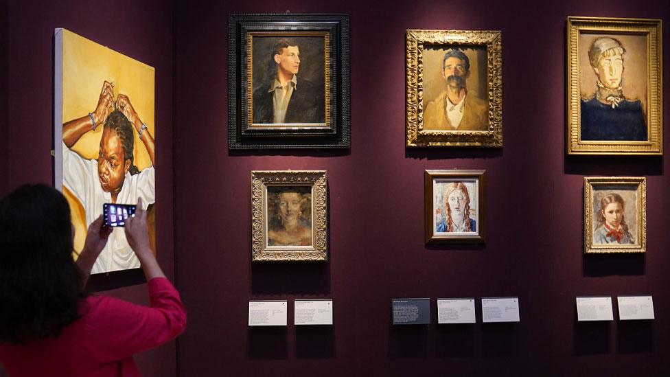 Rebecca Birrell in front of six portraits hung on dark walls at Fitzwilliam Museum, Cambridge