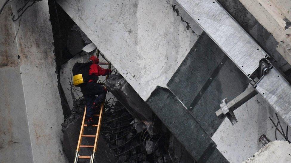 A rescuer climbs a ladder up into large slab of road concrete