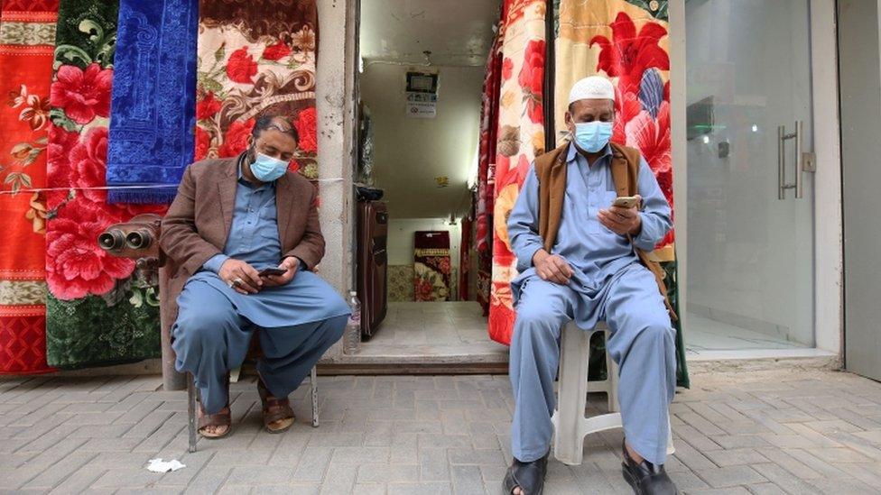 Vendors, wearing protective masks, sit outside their shop in Kuwait City on 26 February