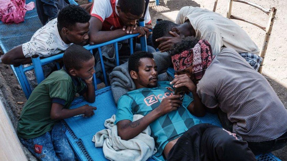 Ethiopian refugees gathering around someone's phone in Hamdayet, Sudan - 8 December 2020