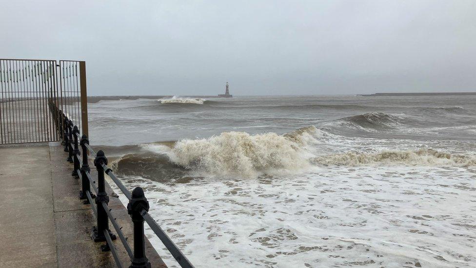 Waves crashing with lighthouse on the horizon