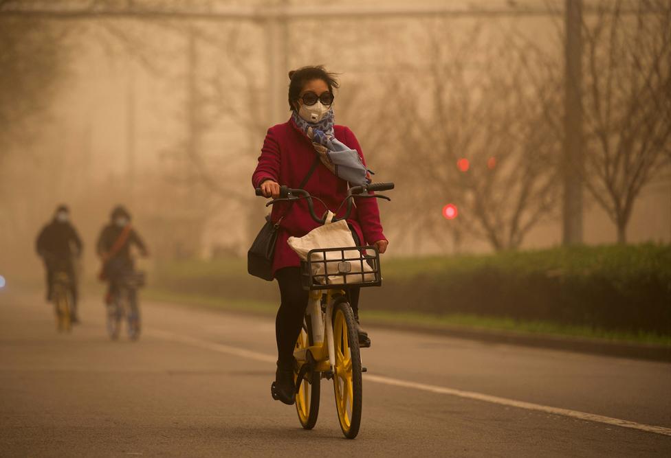 A woman cycles along a street during a sandstorm in Beijing on 15 March 2021