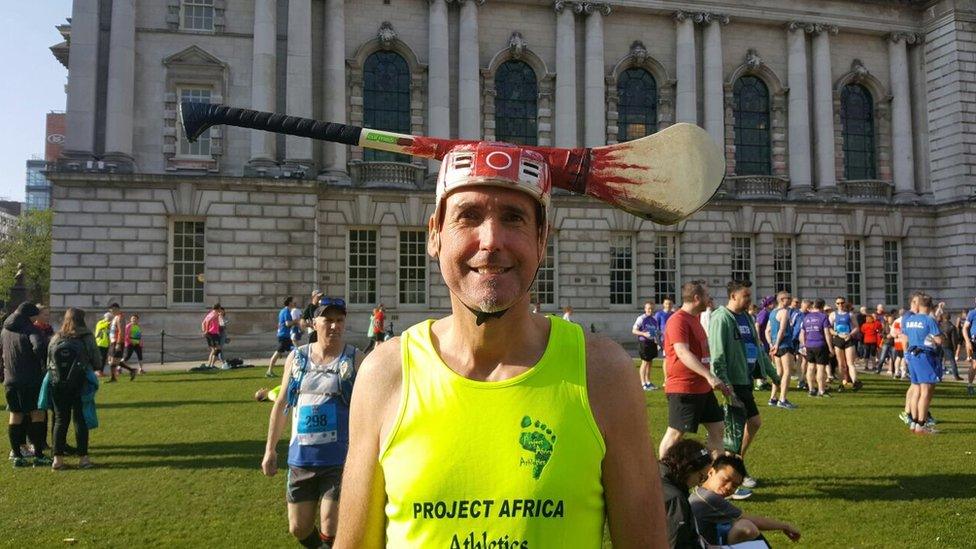 Paul Boyle wears a hard hat with a hurling stick on top outside Belfast City Hall, Belfast City Marathon, 1 May 2017