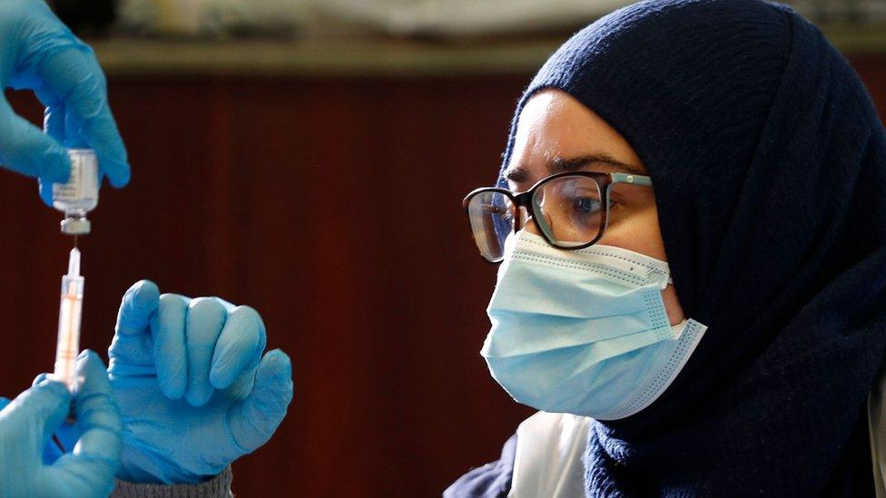 Woman looks at someone else measuring the Oxford-AstraZeneca vaccine in a vial