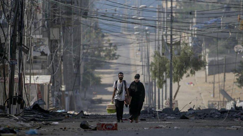 A Palestinian man and his mother leave following an Israeli air strike in the west of Jablaiya refugee camp, northern Gaza Strip, following an Israeli air strike, 11 October 2023