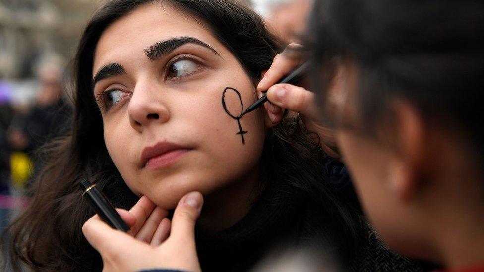 A woman draws a Venus symbol on another woman's face as they attend a demonstration during a one-day strike to defend women's rights on International Women's Day in Barcelona, on 8 March 2018