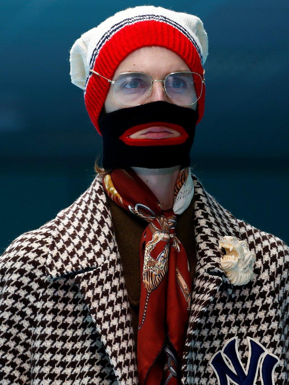 A model wearing a balaclava, brown cravat, lion brooch