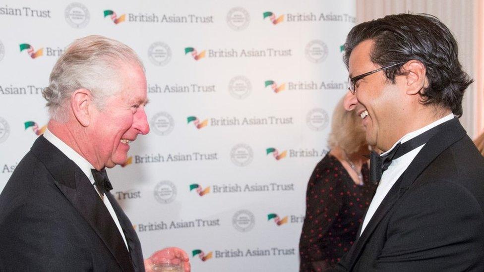 King Charles smiles at Shahzada Dawood in front of a British Asian Trust sign