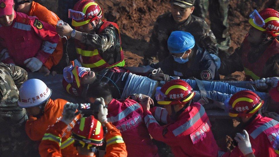 The rescued man, being led away from the site on a stretcher, surrounded by emergency services personnel