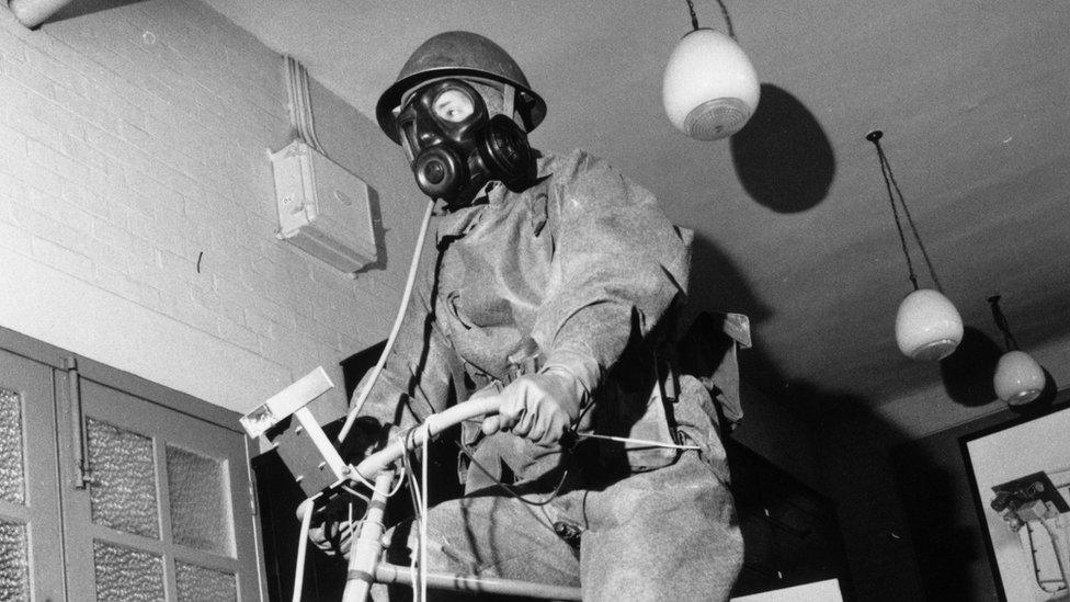 23rd May 1964: A soldier testing a respiratory mask and protective suit by pedalling on a fixed bicycle at the chemical defence establishment at Porton Down, Wiltshire