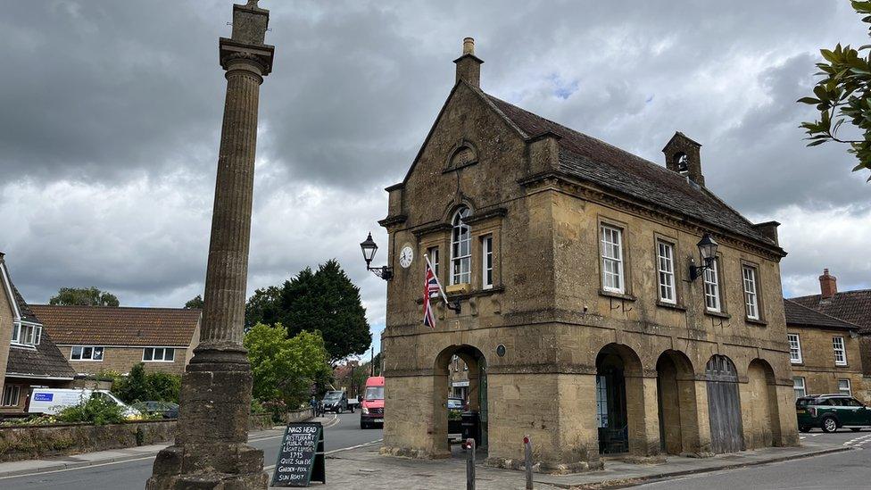 a cream stone building next to a tall stone pillar and a cloudy sky