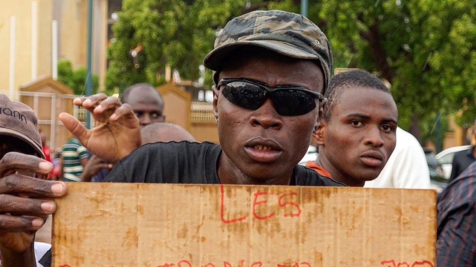 A man holds a sign during a rally in Niger which reads "foreign (military) bases get out"