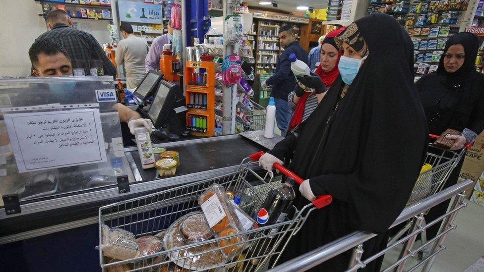 A woman waits at the till of a supermarket in Baghdad before the start of a curfew