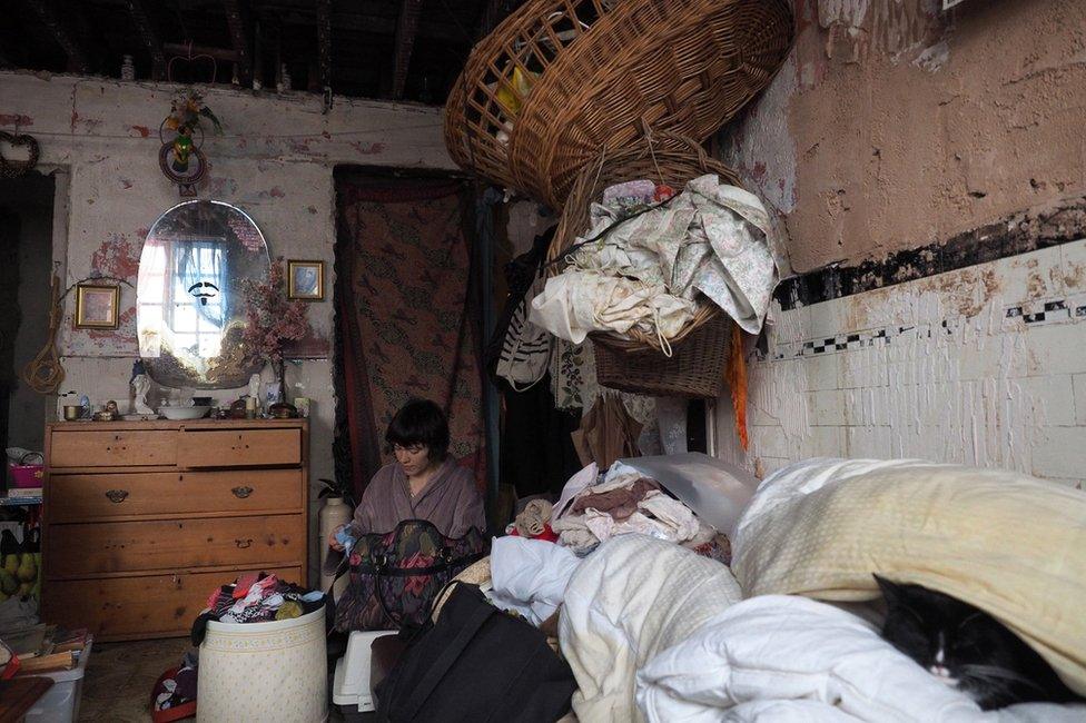 A woman sat alone in a room surrounded by furniture and hanging baskets