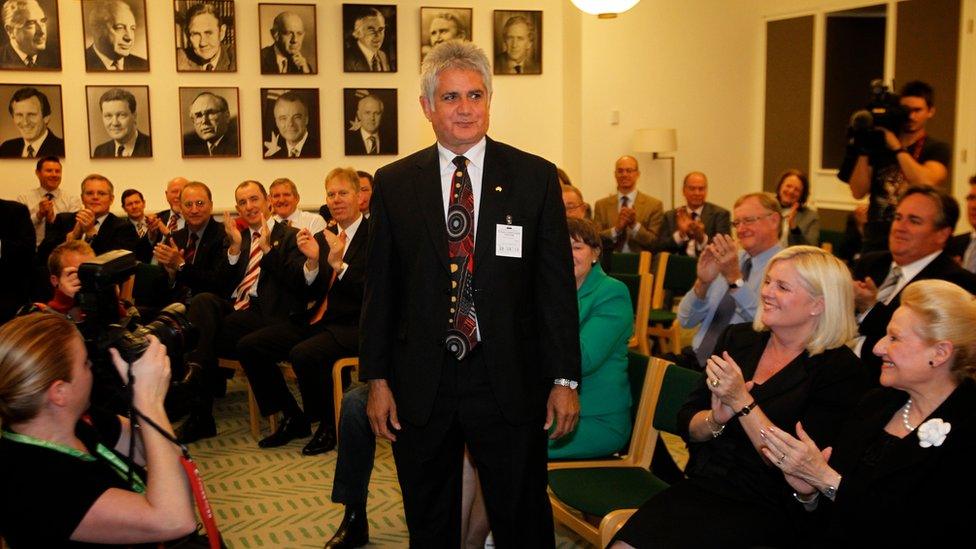 Ken Wyatt stands up in the Liberal party caucus room as other party members applaud