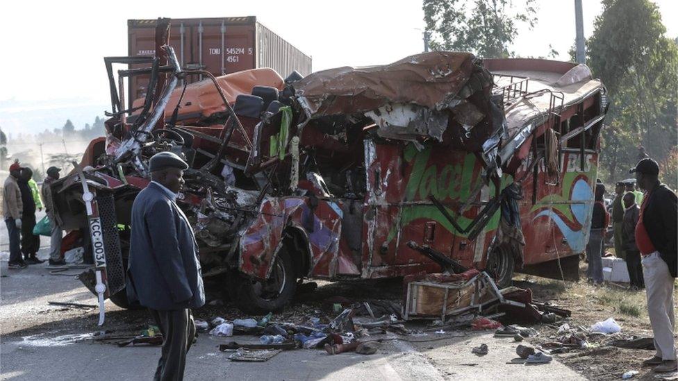 The bus, turned on the right side, is shown heavily damaged and crushed