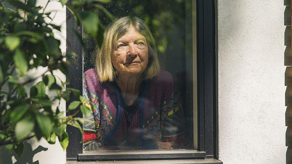 Older woman looking out of her window