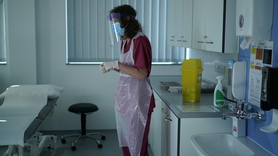 A nurse wearing protective equipment prepares to administer a vaccination