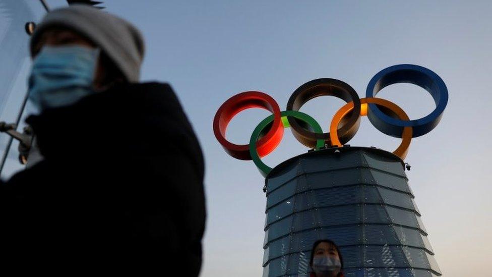 People wearing masks walk by the Olympic Tower in Beijing