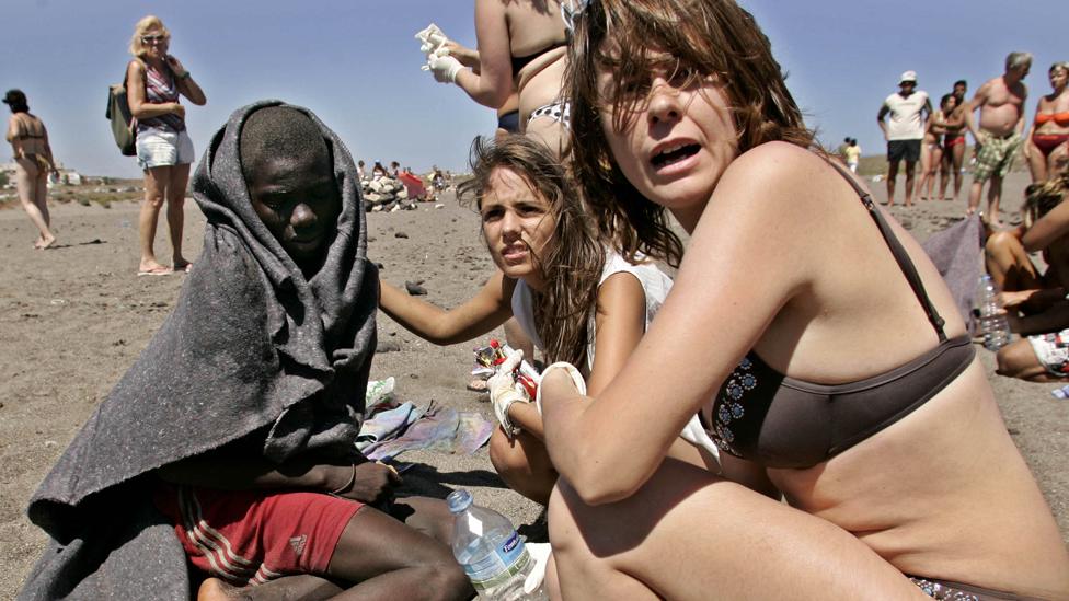 Tourists help a migrant boy on La Tejita beach, Tenerife