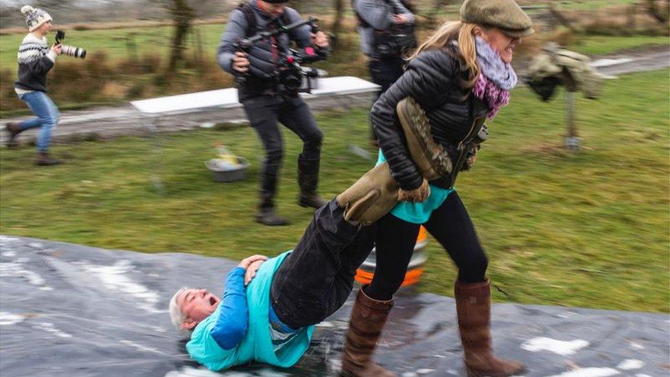 Woman drags a man along the ground covered in a slippery, wet plastic