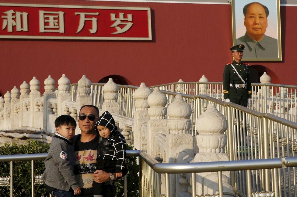 A man carrying his children in his arms poses for photograph in front of the giant portrait of late Chinese chairman Mao Zedong on the Tiananmen Gate in Beijing