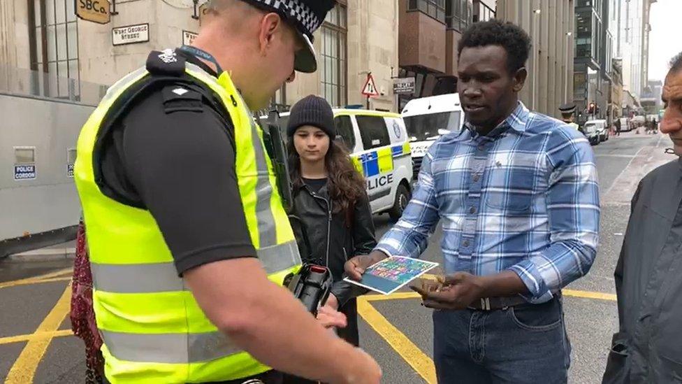 Asylum seeker passing a get well card to police officer