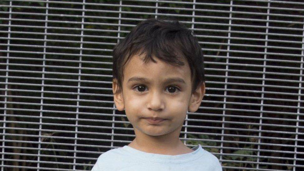 Two-year-old George stands before a fence on the island of Nauru