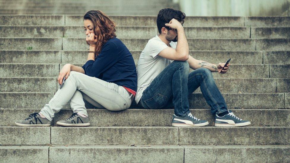 teenage couple sitting back to back on phones