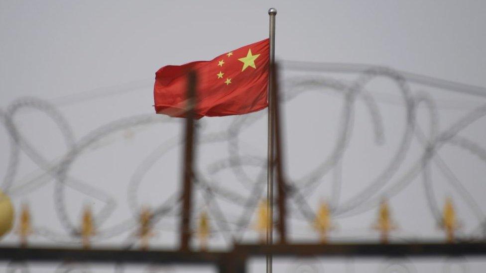 a Chinese flag waves behind a fence covered in barbed wire