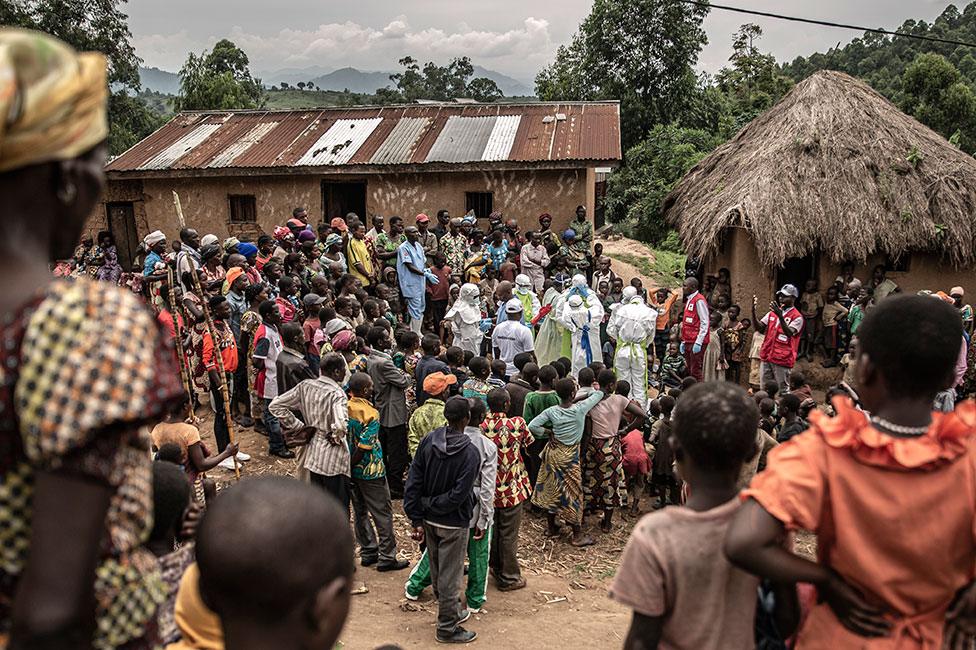 Neighbours and Red Cross burial workers in protective clothing gather outside a home