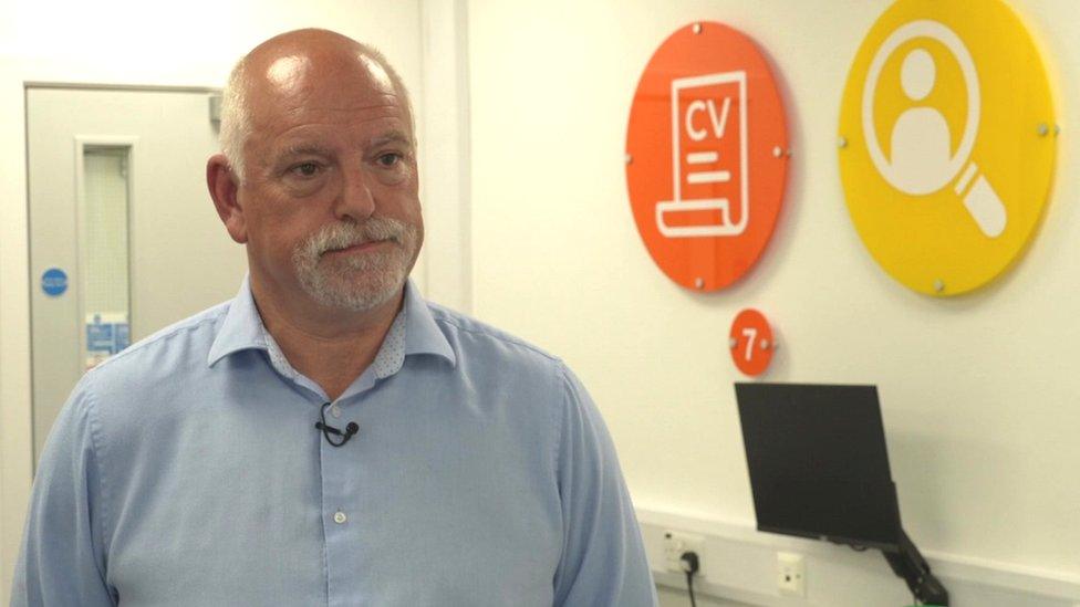 Alun Roberts in the Mon CF office beside a computer monitor and signs